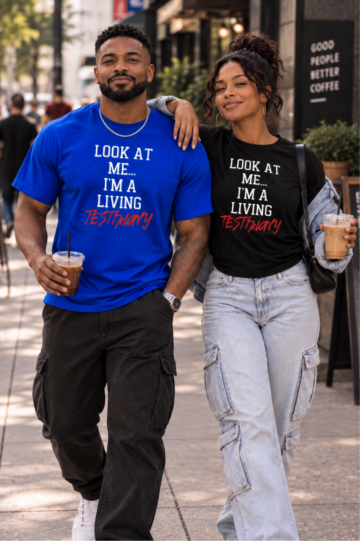 A man and a woman walking arm-in-arm on a city sidewalk, both wearing matching graphic T-shirts with the text 'LOOK AT ME.