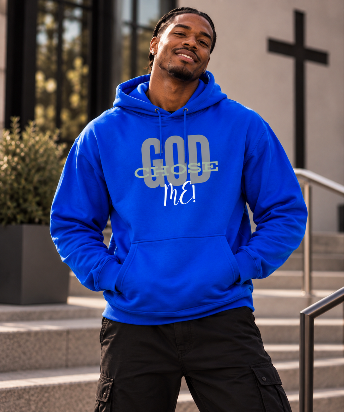 A man wearing a bright blue hoodie with the text 'GOD CHOSE Me!' printed on the front, standing on outdoor steps in front of a building with a cross in the background.