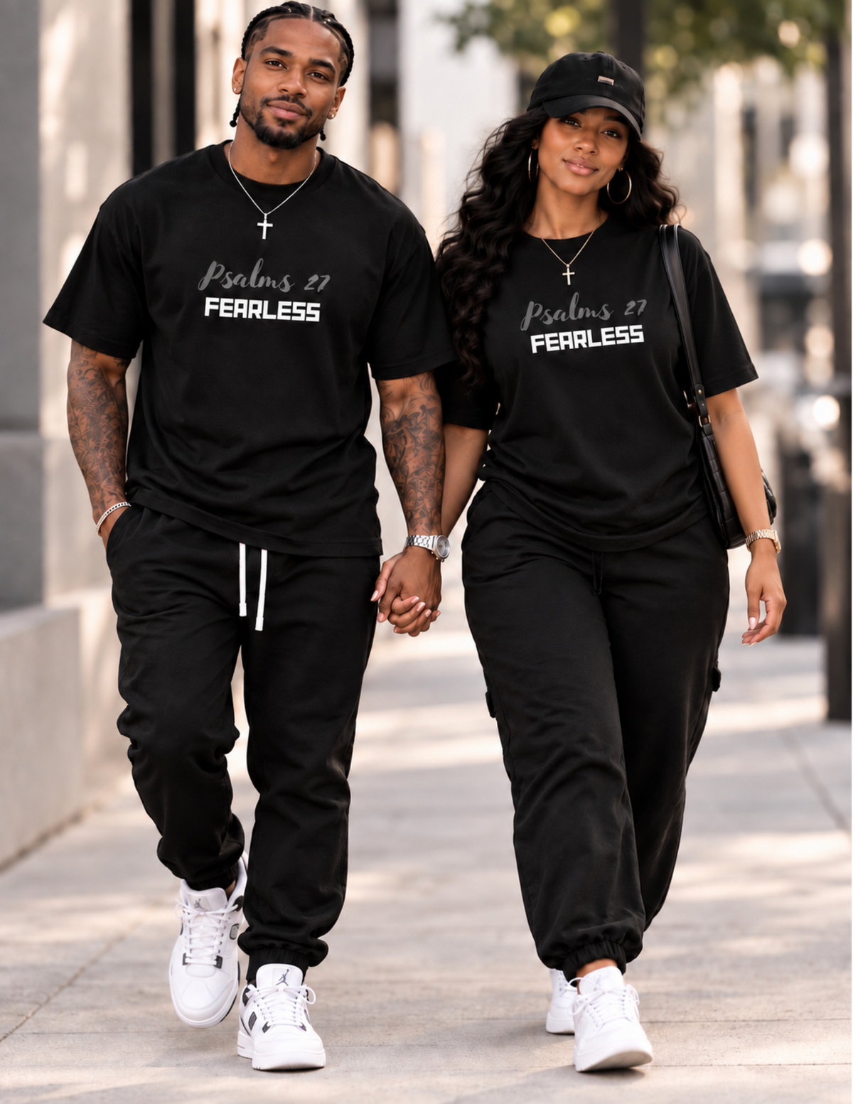 A man and a woman walking hand-in-hand down a city sidewalk, wearing matching black t-shirts with 'Psalms 37 FEARLESS' printed in white on the chest, paired with black jogger pants and white sneakers.